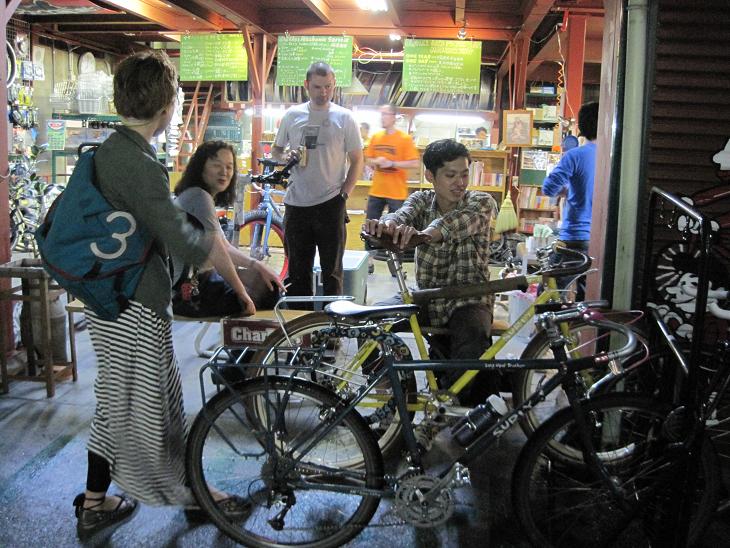Right side view of a Surly Long Haul Trucker bike, in front of an large open door from a bike shop, with people around